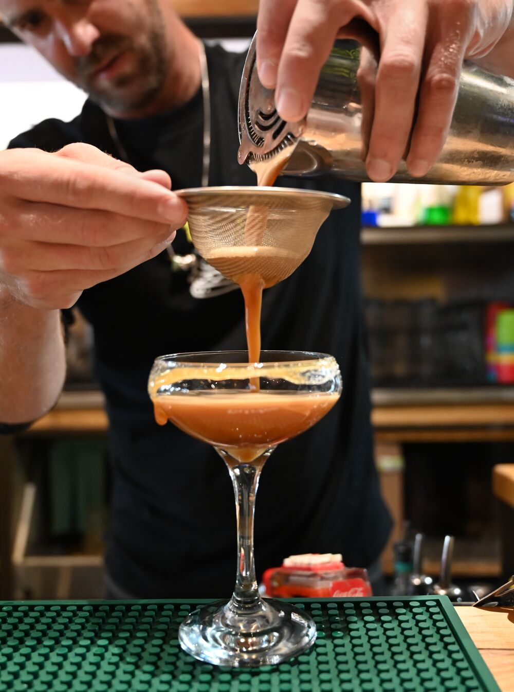 A bartender filters out the parts of a cocktail indoors.